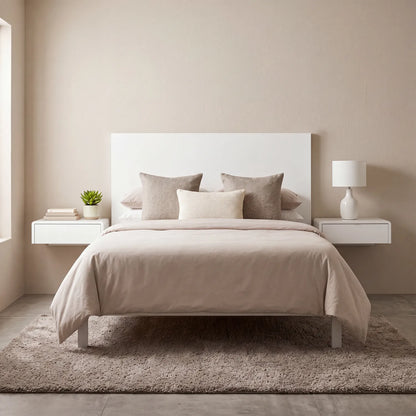 A minimalist beige bedroom featuring a bed dressed in neutral beige and taupe bedding, flanked by two white floating nightstands with matching lamps and a small potted plant.