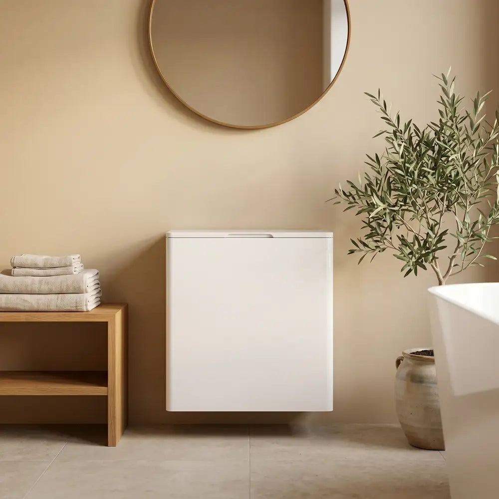 A modern white wall-mounted bathroom vanity or storage cabinet shown in a styled bathroom setting with a round mirror, wooden shelf with folded towels, potted plant, and part of a bathtub visible.