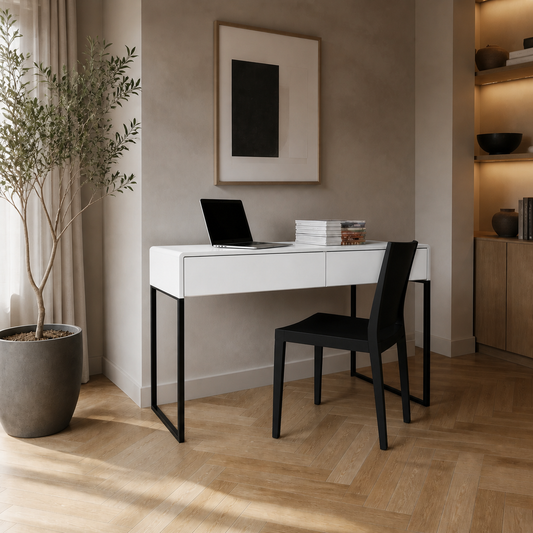 A modern white desk with a black metal frame and a black chair, styled in a minimalist home office setting with a potted plant, framed wall art, and warm ambient lighting.